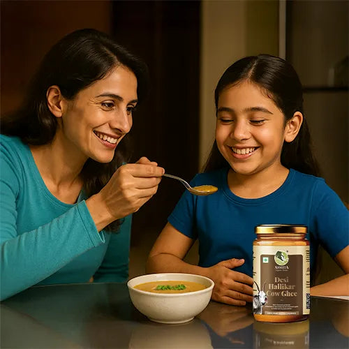 Woman feeding a child with a spoon, both smiling, with a jar of Desi Haldiram food product on the table.