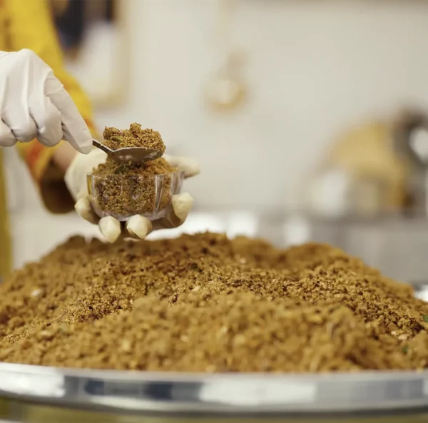 A close-up of the panjiri-making process, showing a gloved hand scooping freshly prepared panjiri into a container.