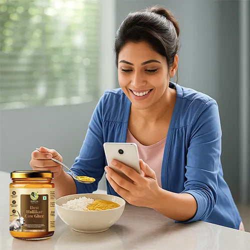 Woman using a smartphone with a bowl of food and a jar of Desi Ghee on a table.