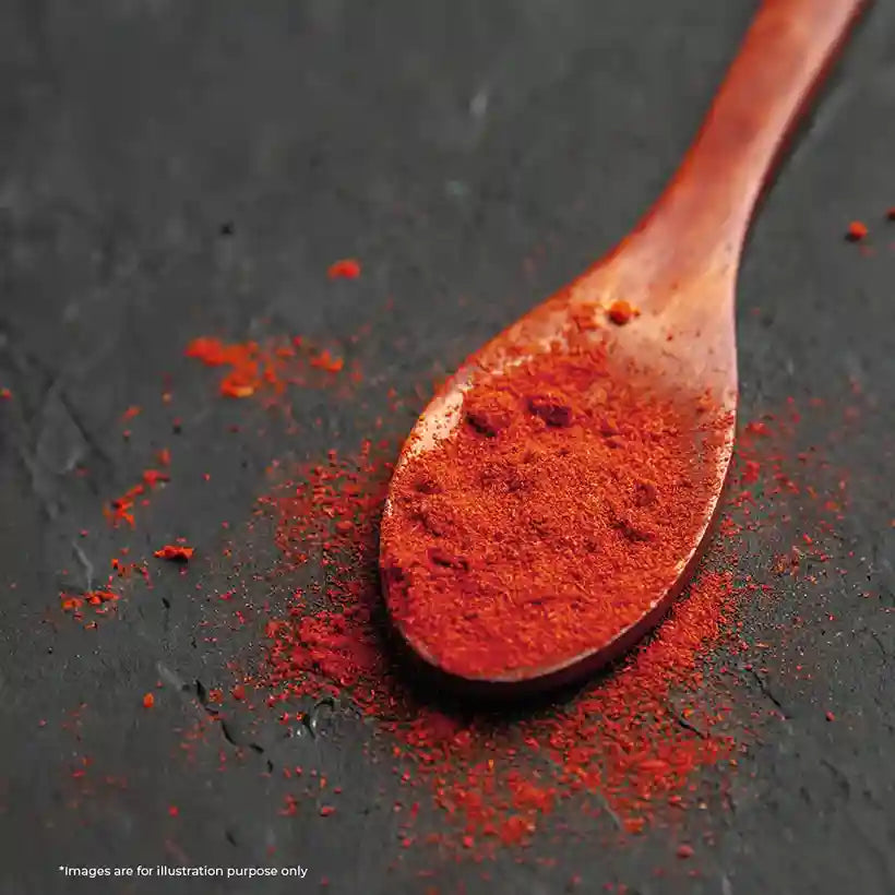 Wooden spoon filled with red chili powder, scattered on a dark textured surface.