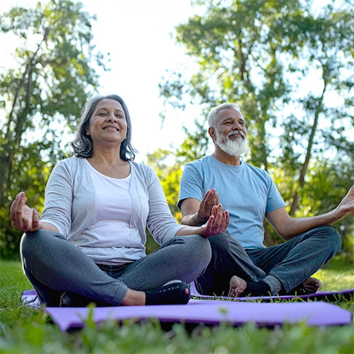 Two elderly people sitting on yoga mats in a park