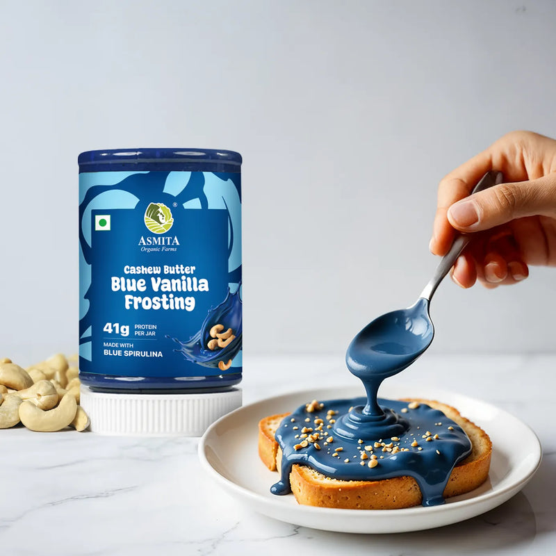 Person pouring blue vanilla frosting from a can labeled 'Asmita' onto a dessert.
