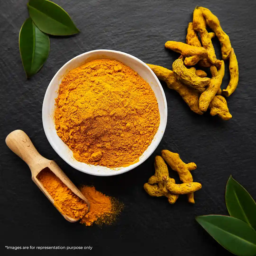 A bowl of vibrant turmeric powder surrounded by raw turmeric roots.