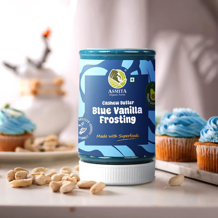 A styled shot of Blue Vanilla Frosting Cashew Butter with cupcakes and cashews, emphasizing its superfood qualities.